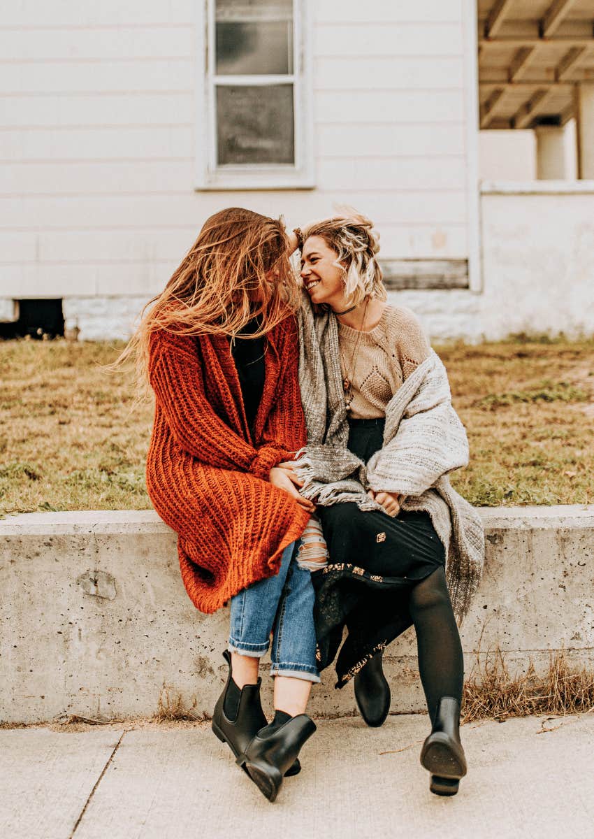 two smiling women sitting close outside