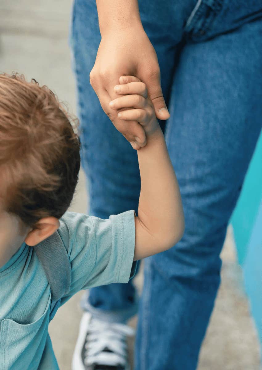 young child wearing a backpack holding on to an adult's hand