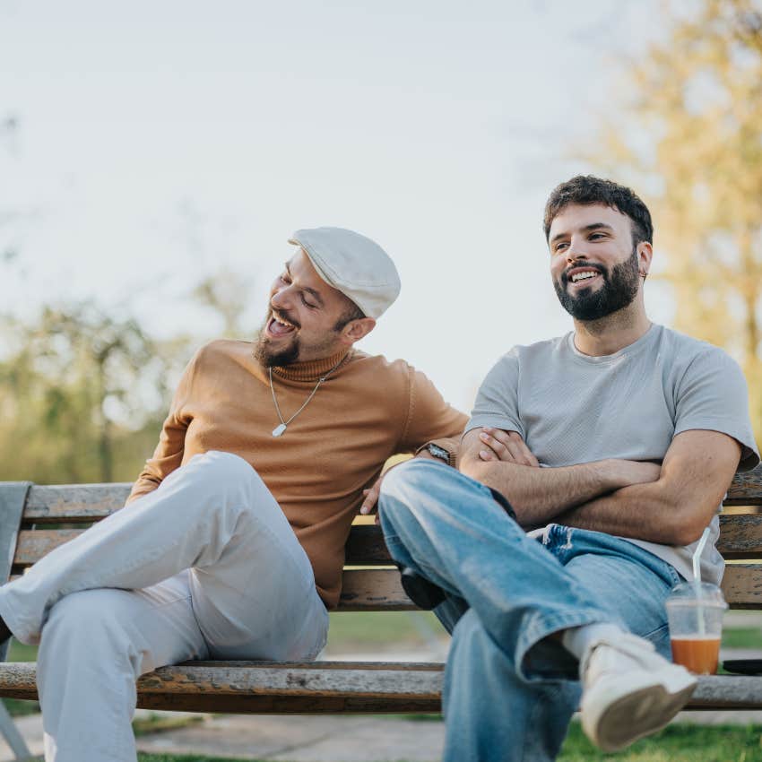 likable man laughing easily with his friend while sitting on a park bench