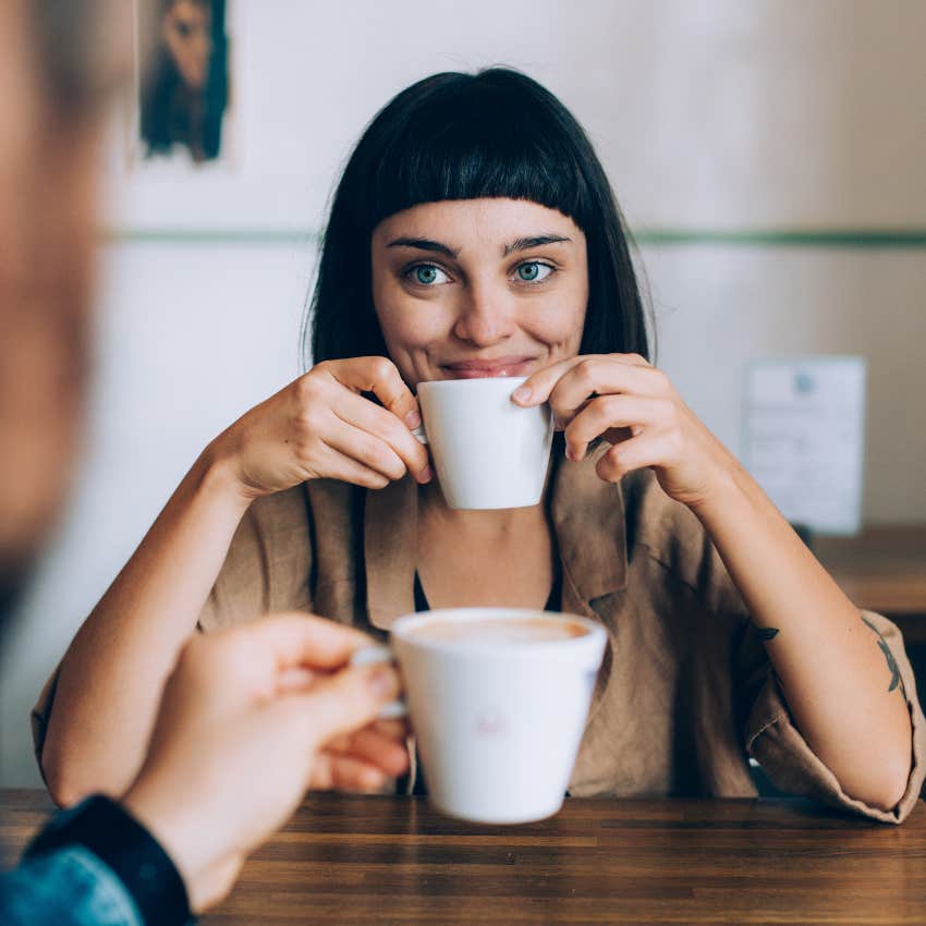 woman drinking coffee smiling while friend talks and saying that's so cool