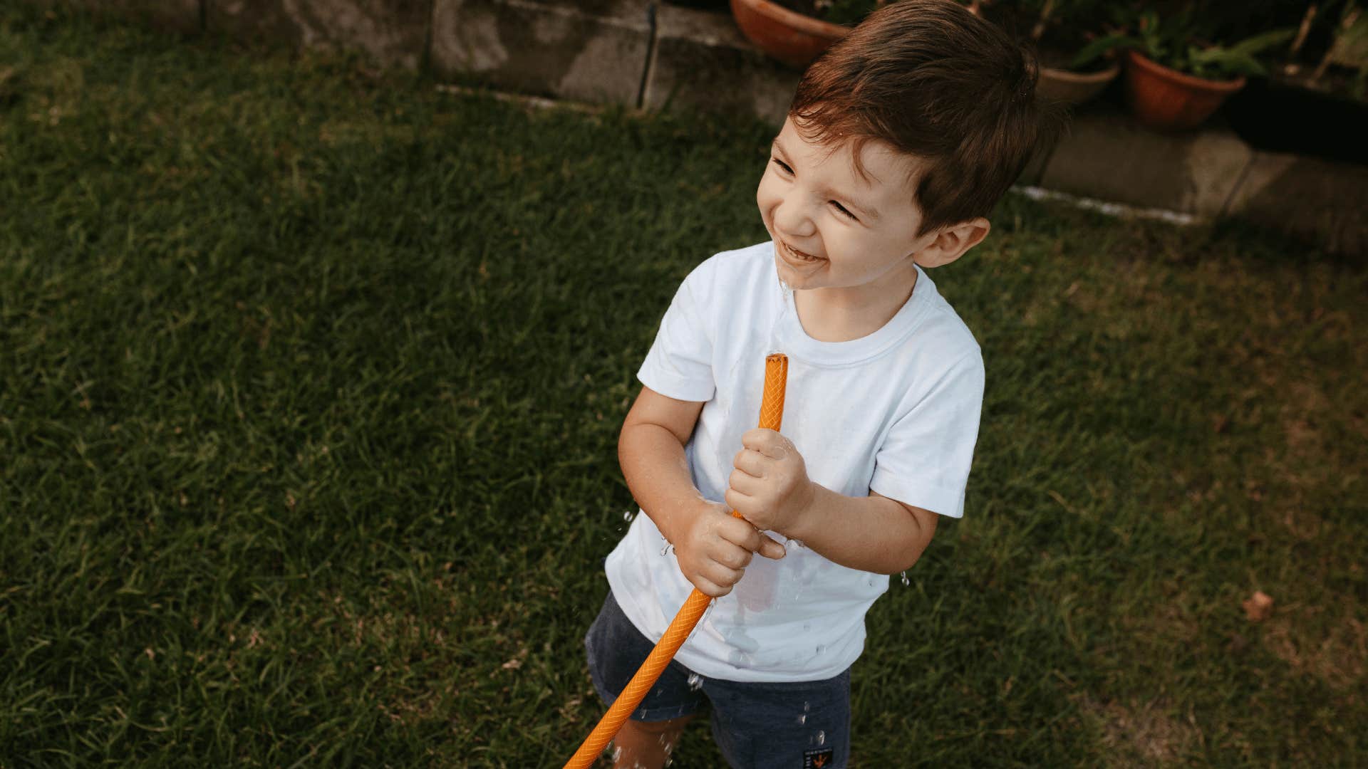 little boy drinking from the garden hose smiling