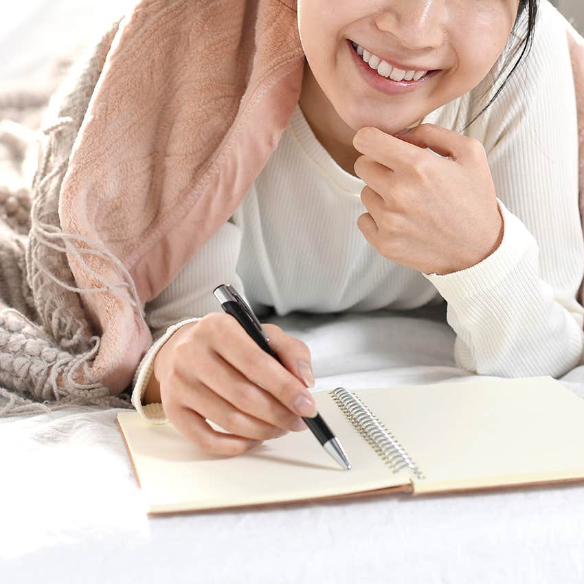 woman writing ideas in notebook while in bed