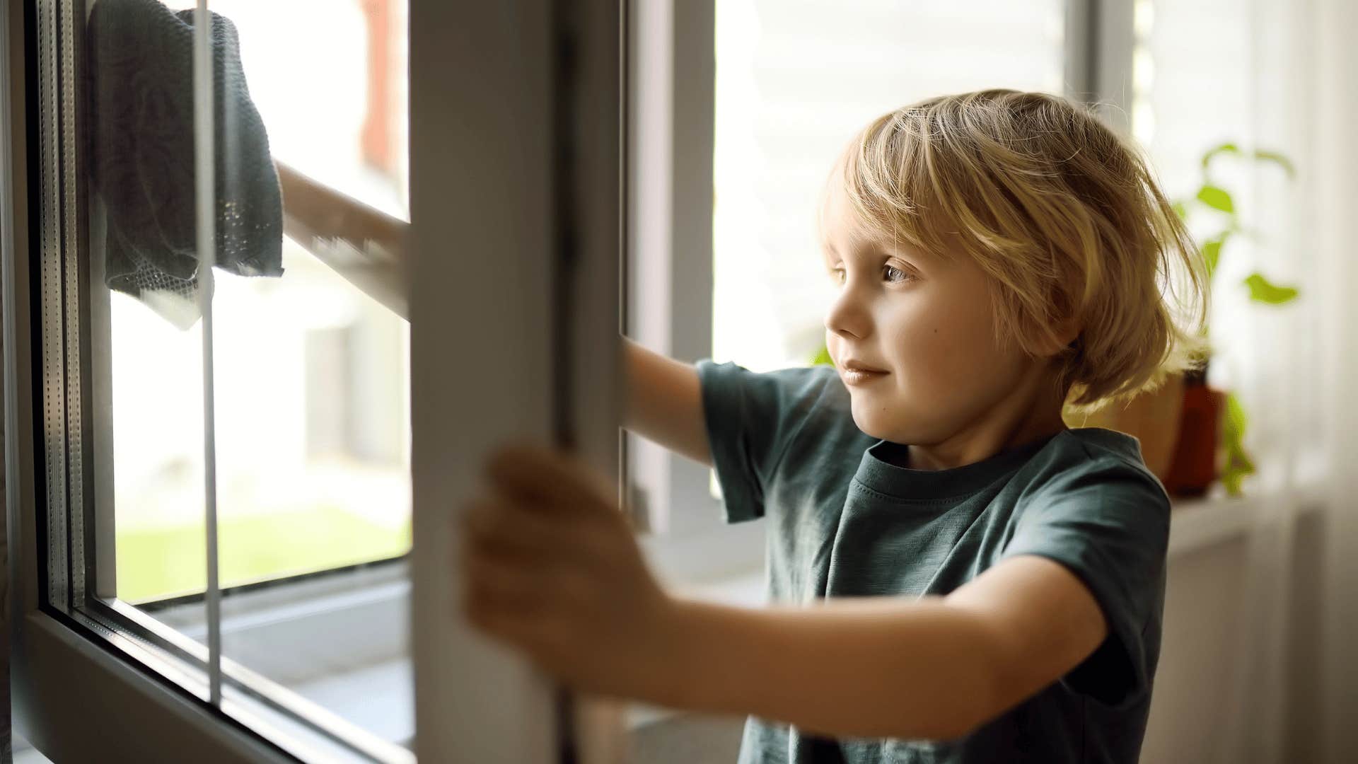 little boy washing the windows at home for his parents
