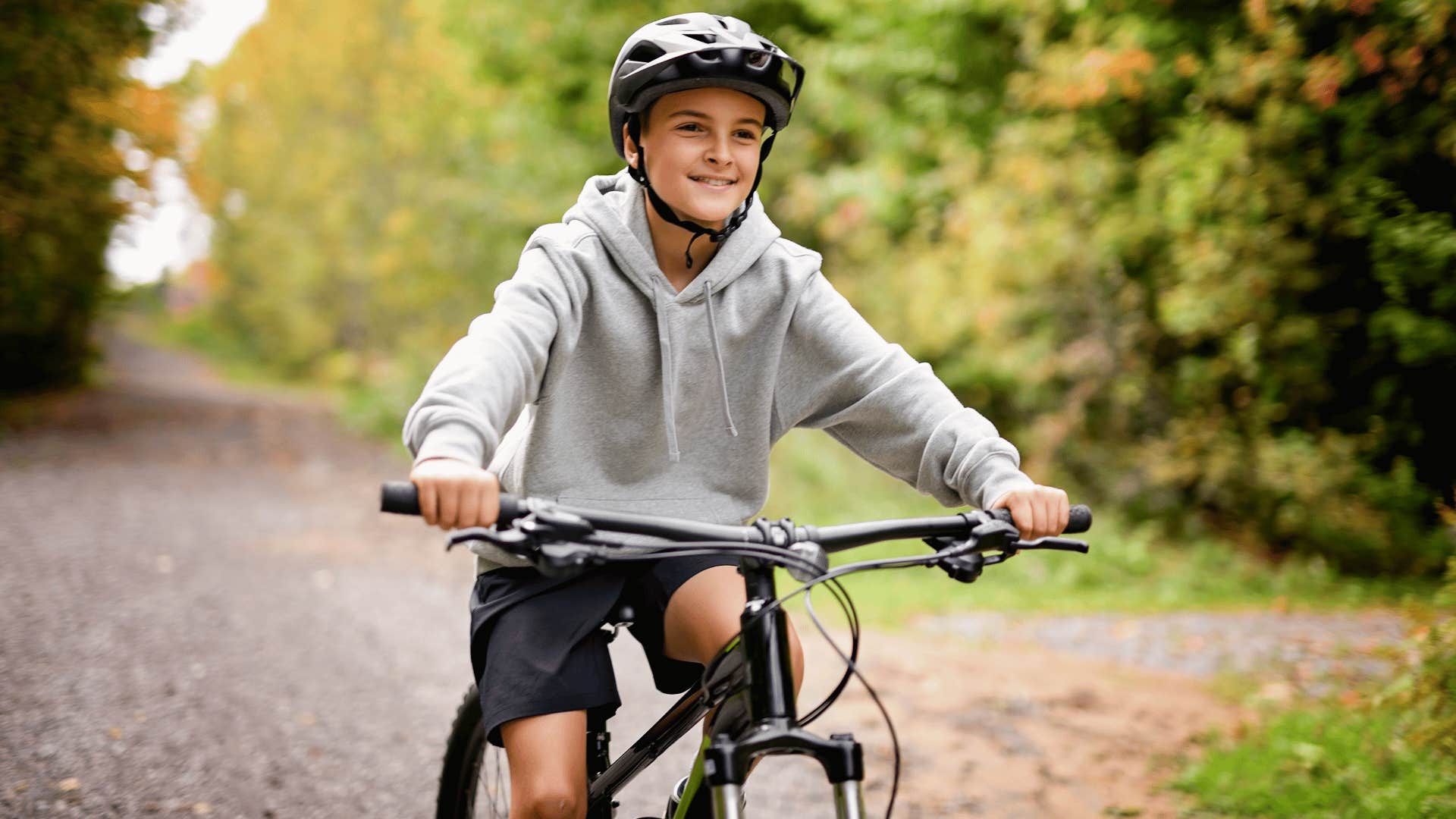 kid in gray hoodie biking with helmet