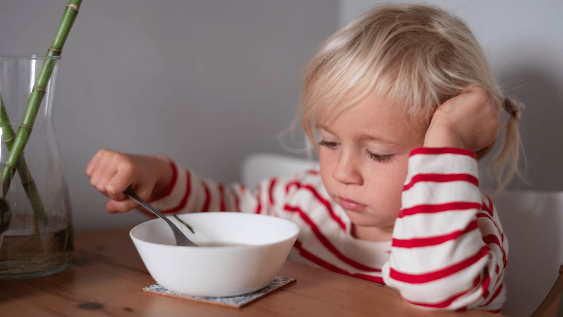 little girl who has to clean her plate at dinner eating soup