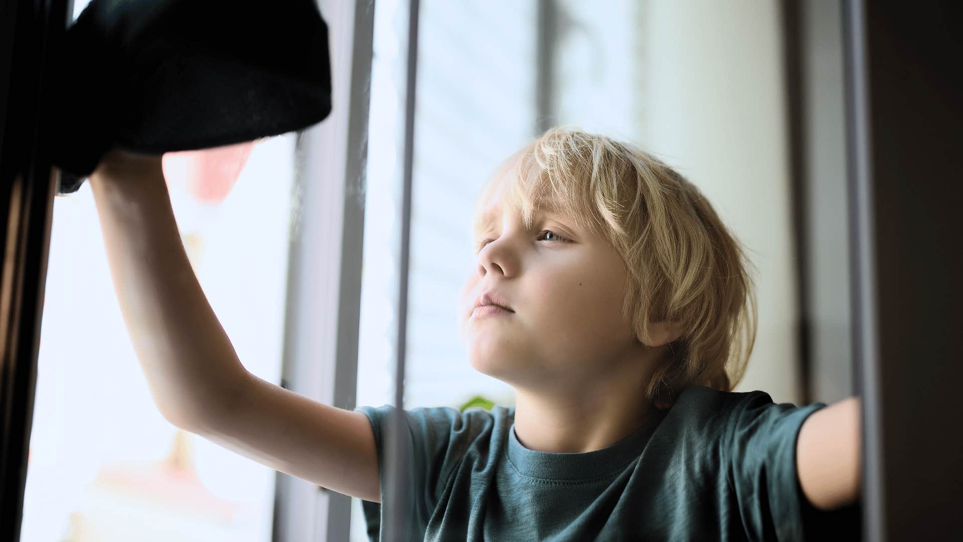 little boy doing household labor cleaning the windows