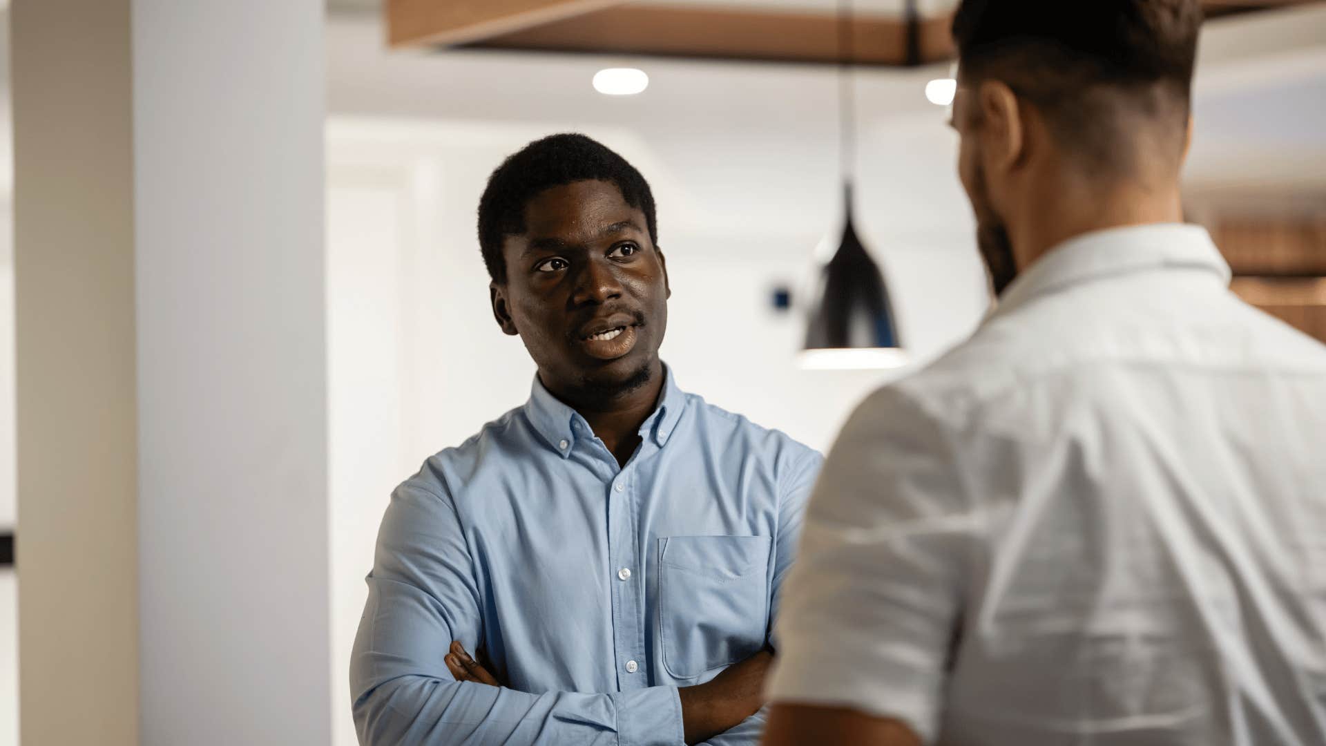 man in blue shirt crossing arms as he tells coworker i'm not good at that