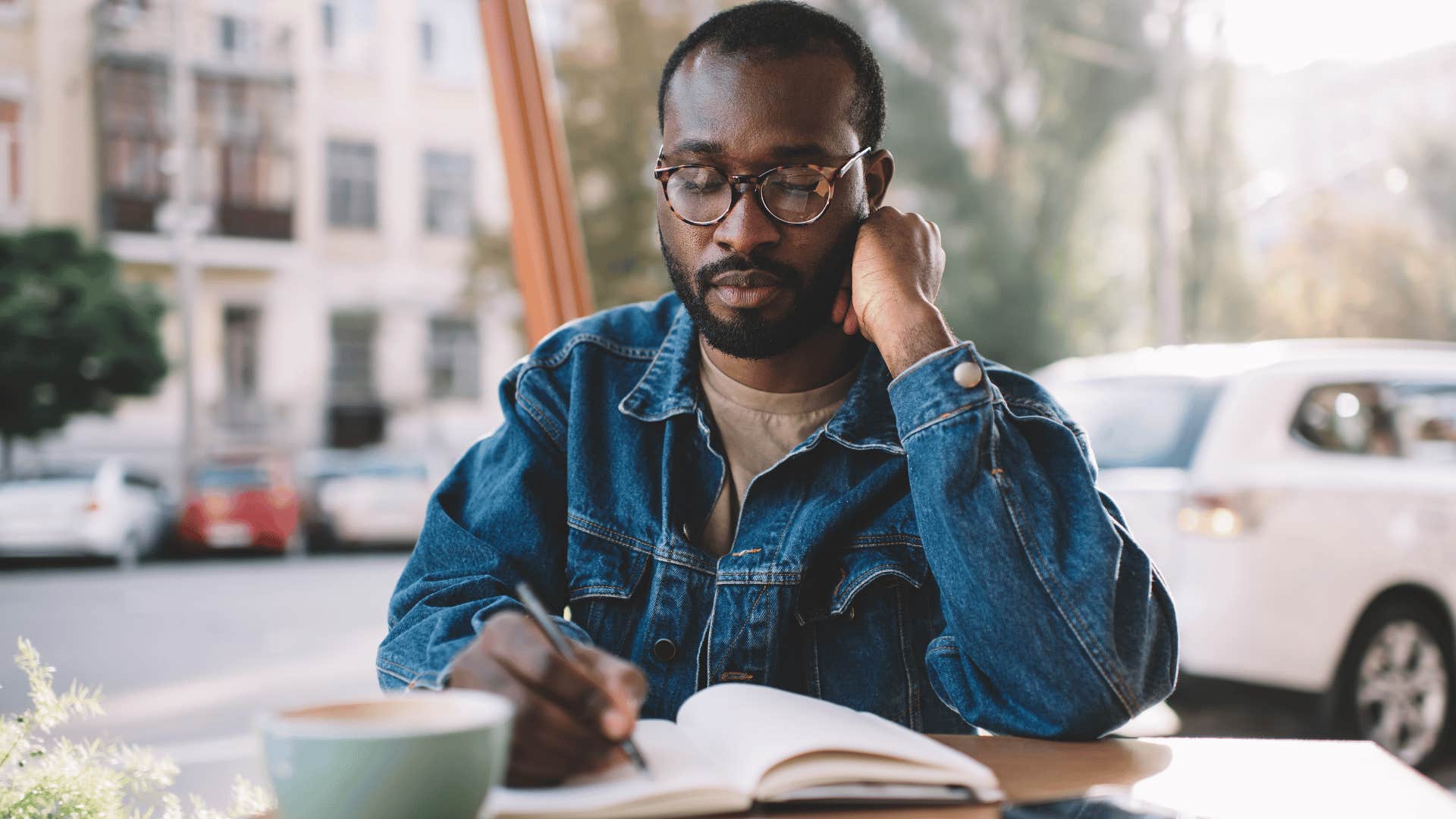 man in jean jacket journaling their thoughts and everyday life at cafe
