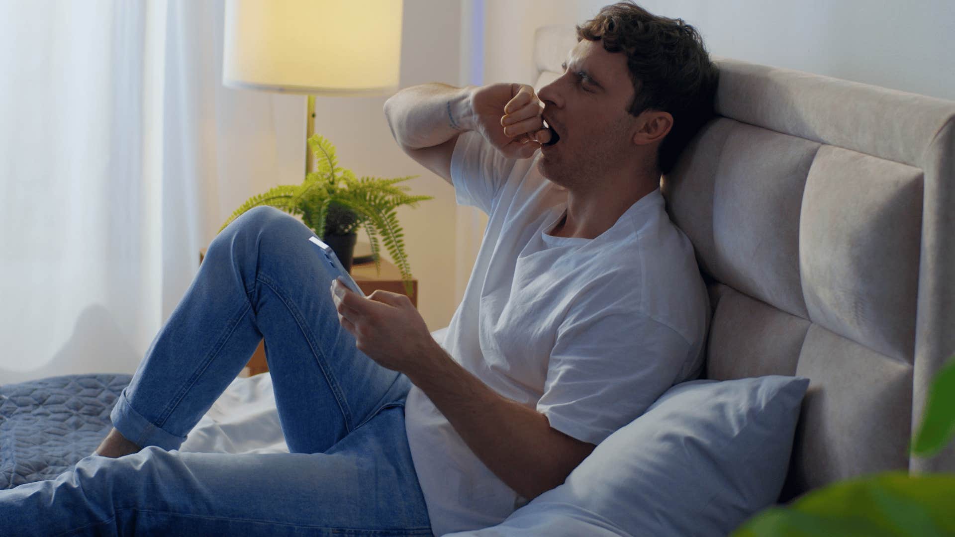 man neglecting basic self-care yawning in bed