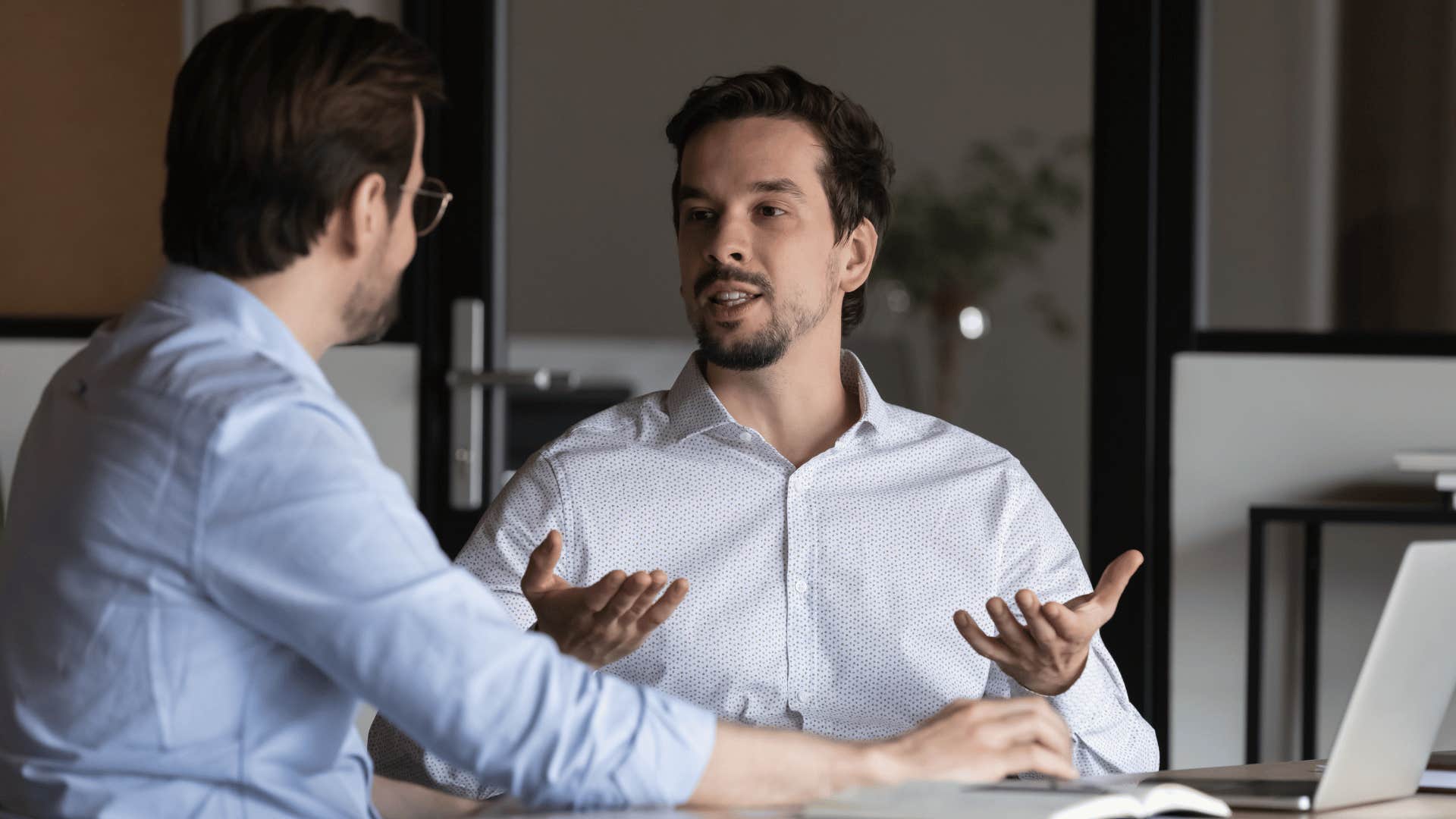 man in white shirt telling coworker i don't want to make assumptions at meeting