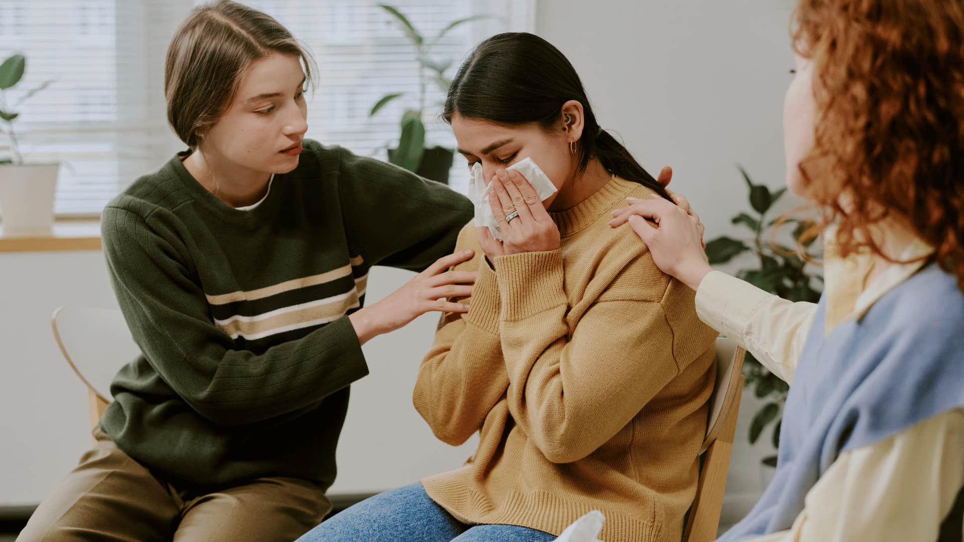 woman in brown shirt crying as friends comfort her and ask her how can i help