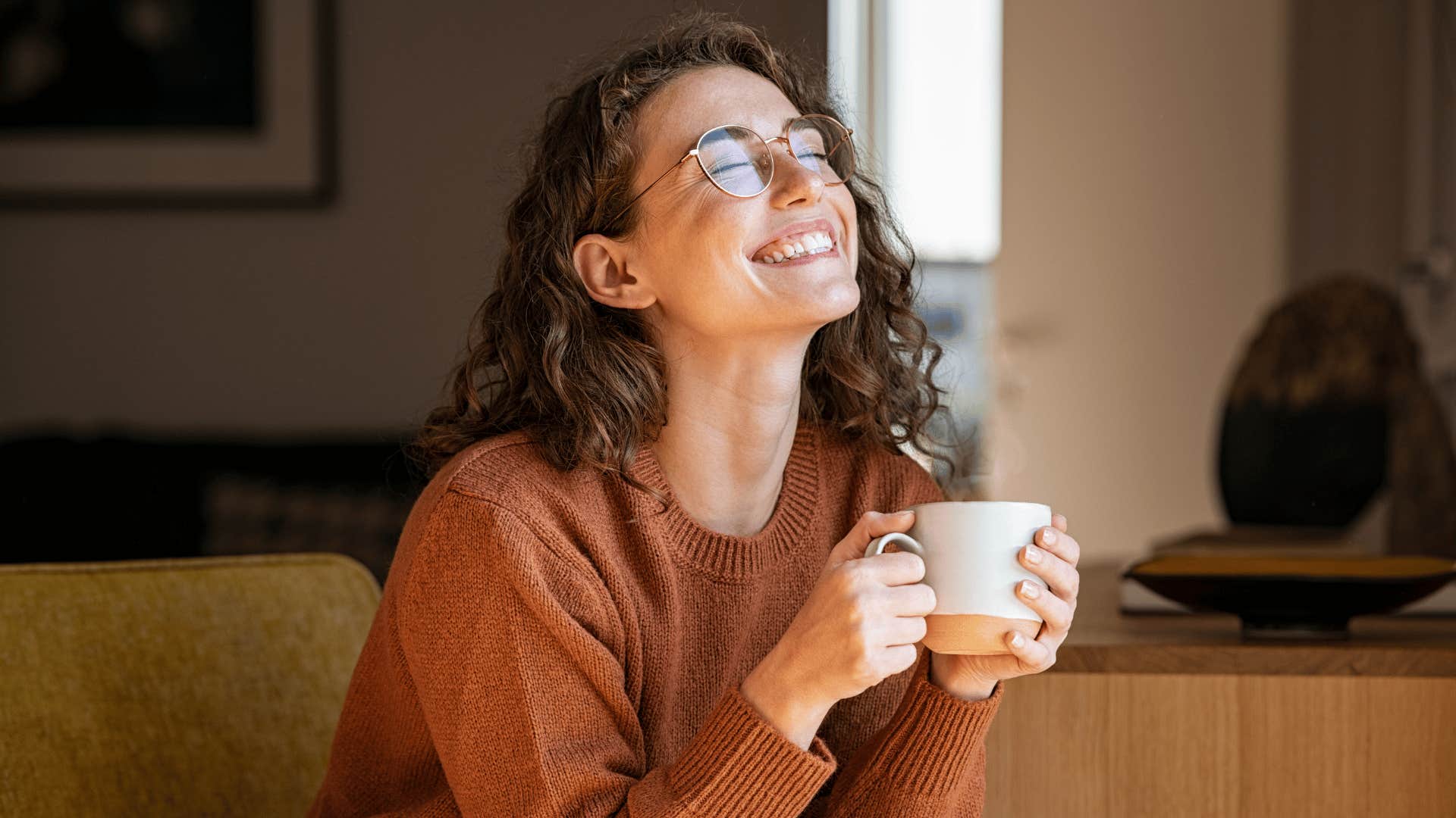 woman in brown shirt smiling brightly with coffee in hand as she thinks i'm grateful for what i have