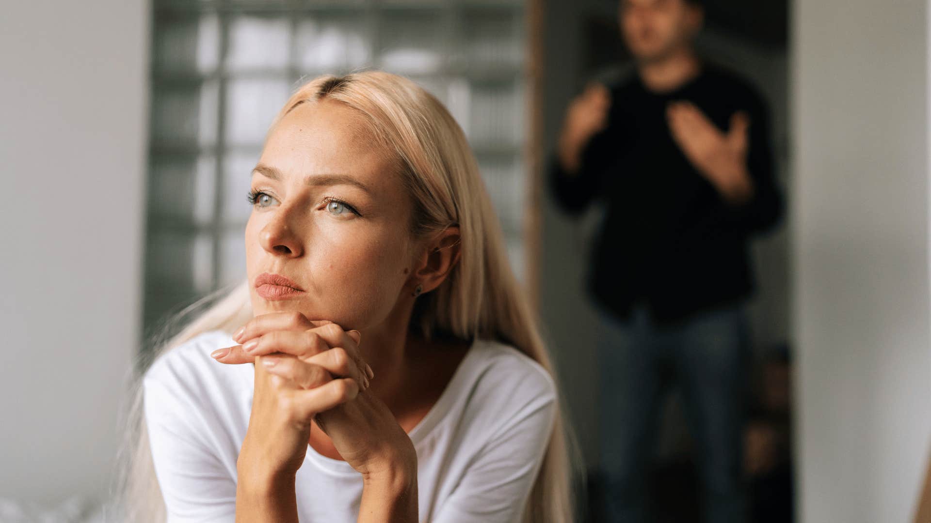 woman in white shirt thinking deeply as man behind her yells i shouldn't have to explain myself