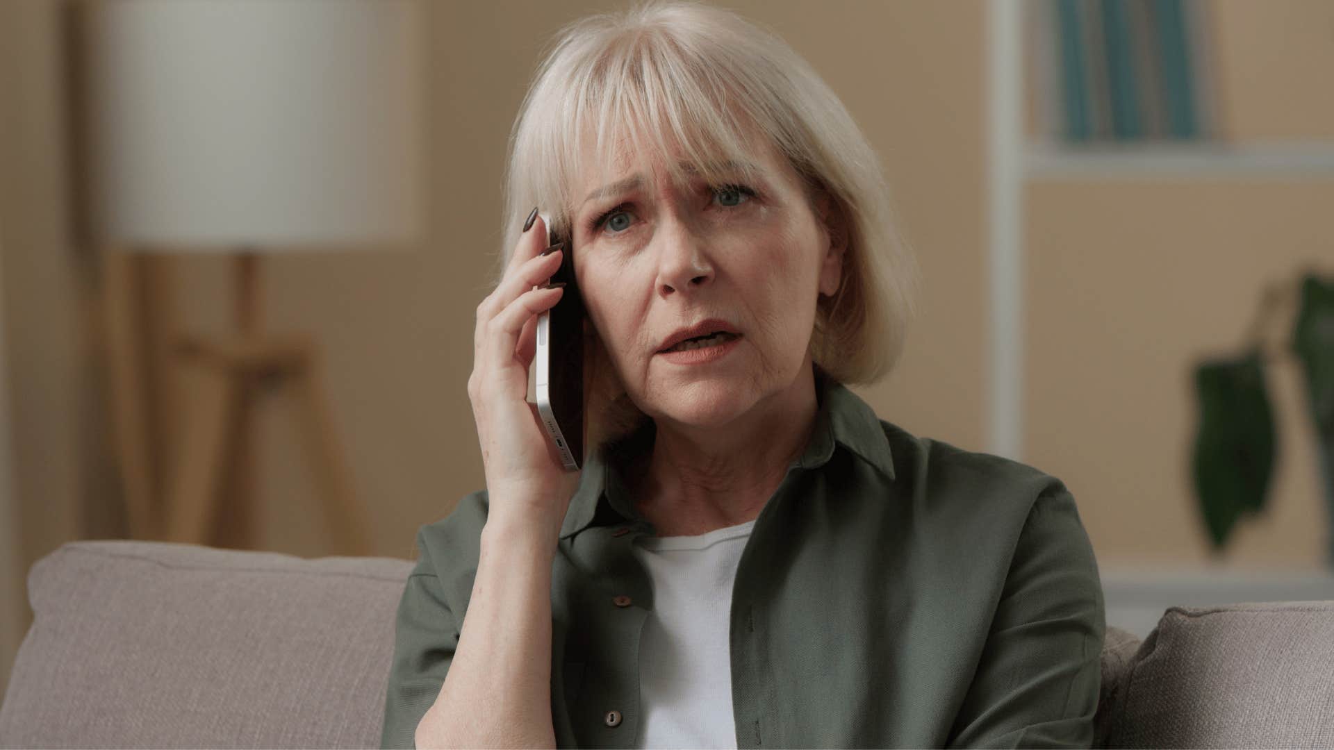 woman in green jacket on the phone looking confused as she says i don't need to apologize