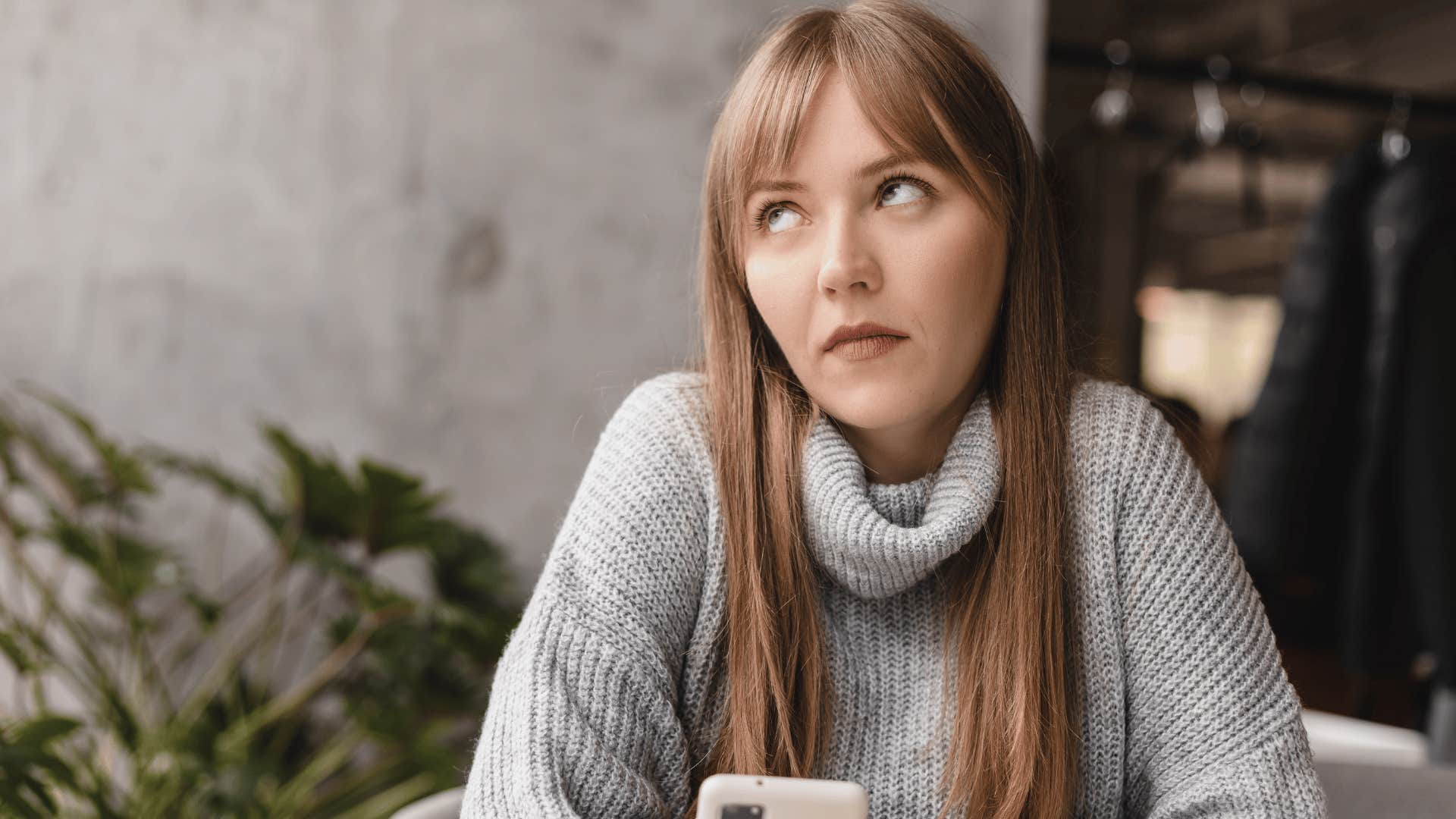 woman in gray sweater looking annoyed at phone as she thinks people are so sensitive nowadays