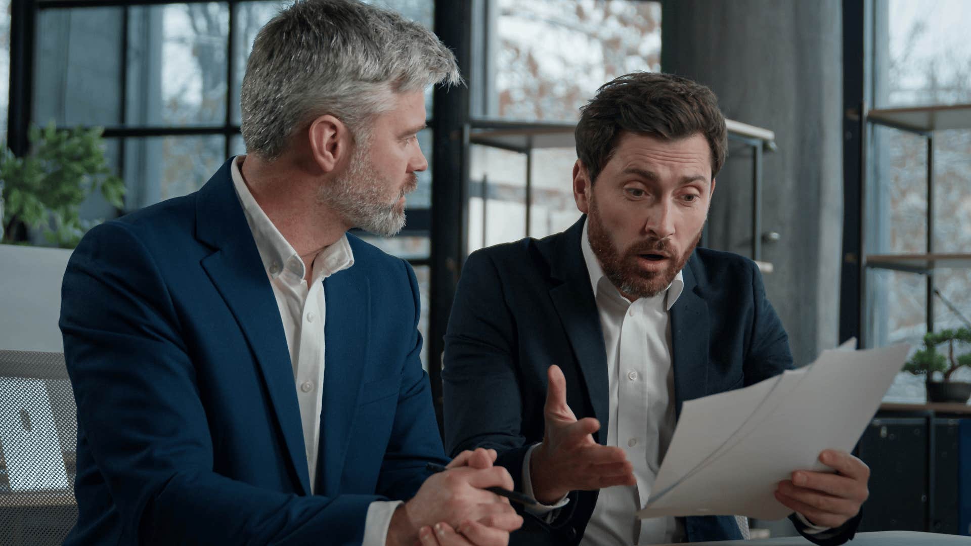 coworker looking over documents stressed as man in blue suit thinks that's not my problem