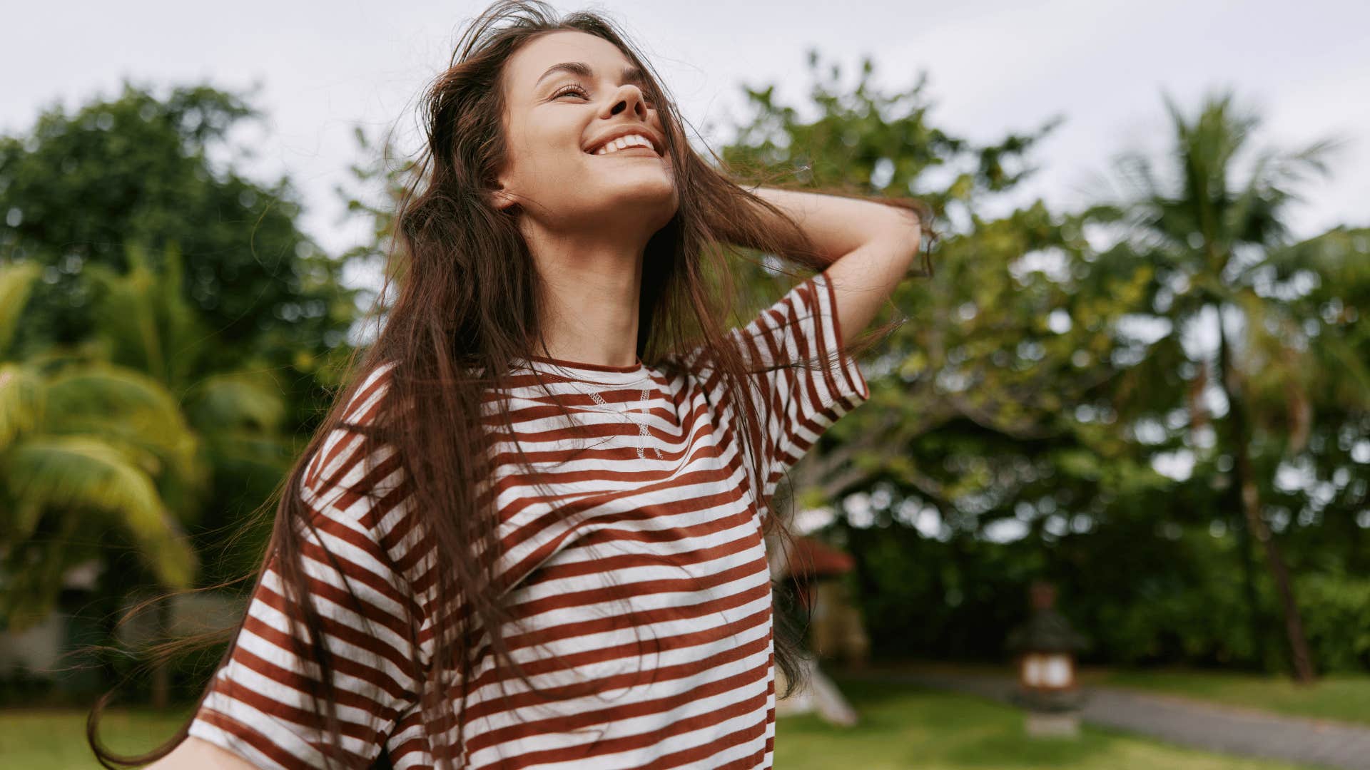 woman in stripped shirt smiling brightly as she isn't too hard on herself
