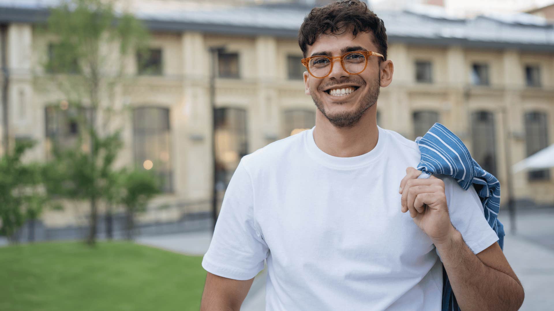 man in white shirt smiling brightly in front of university as he thinks i can handle it