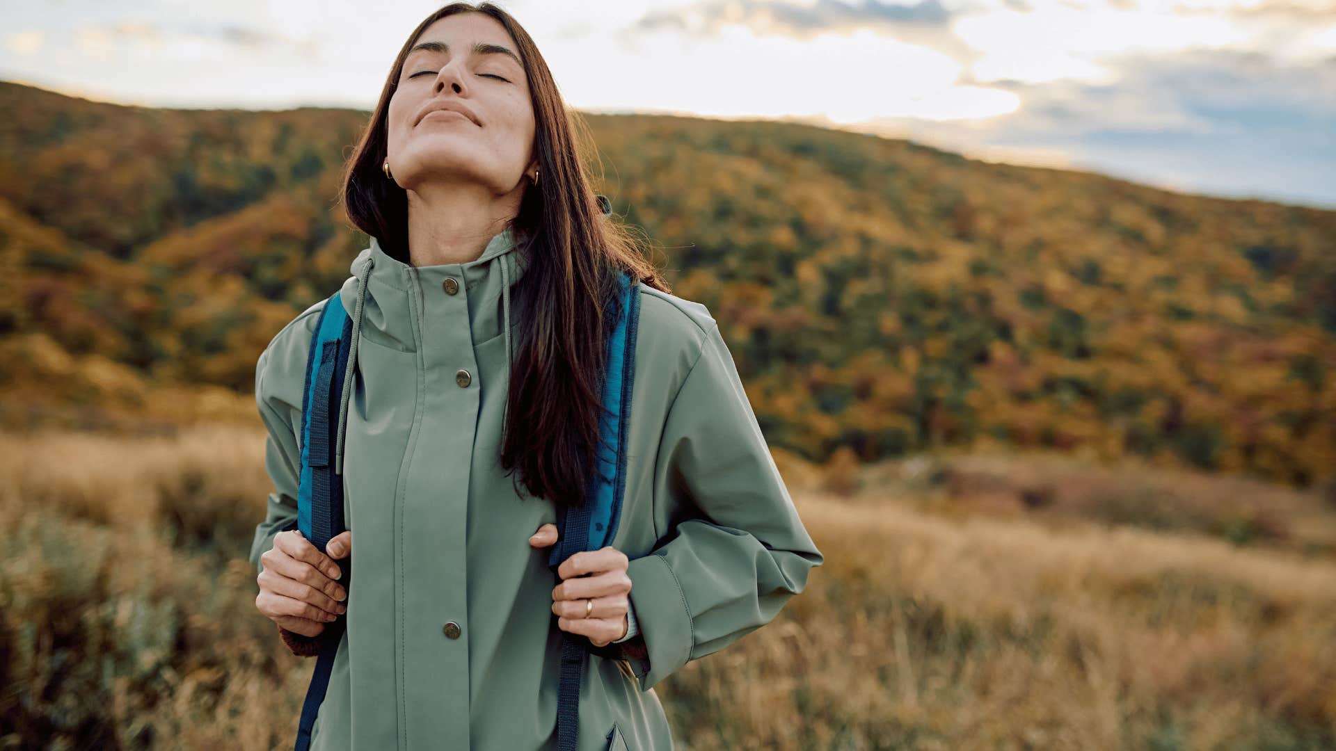 woman in green jacket hiking and deep breathing as she thinks it's never too late to start over