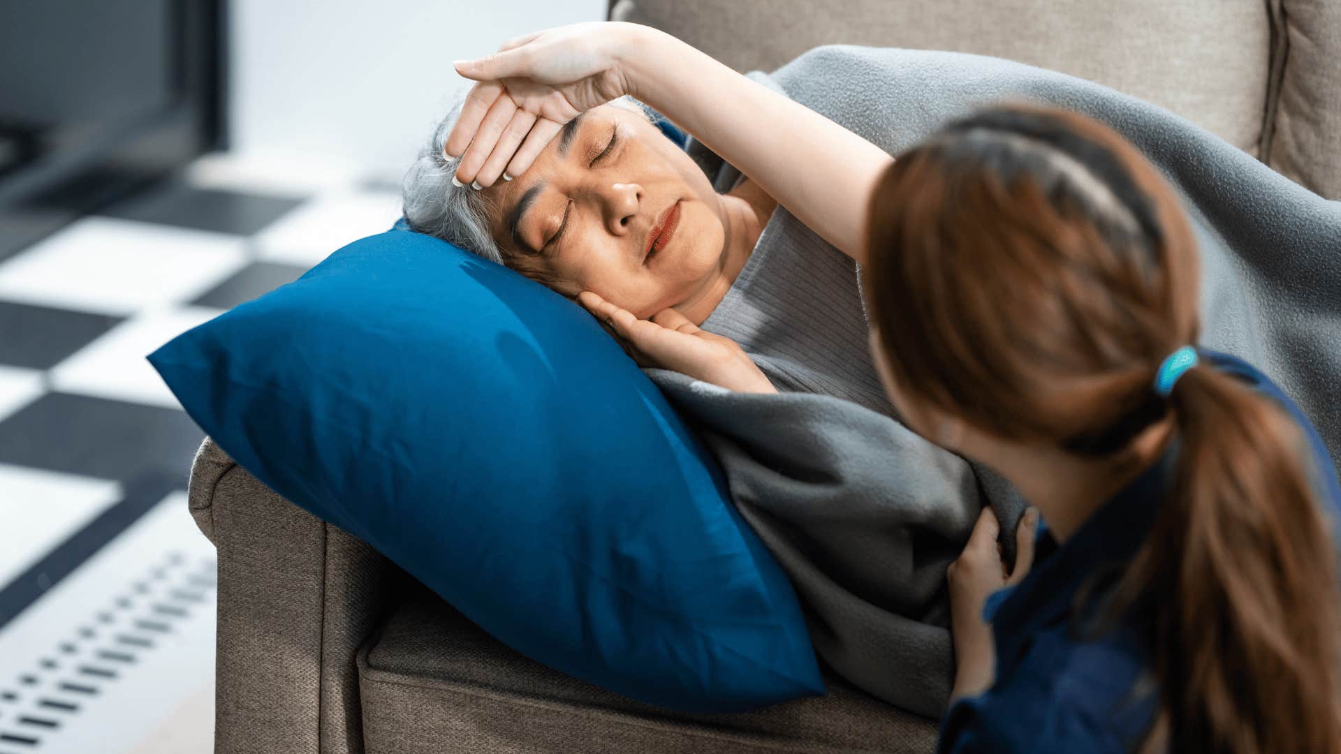 woman checking older woman's temperature caring for her