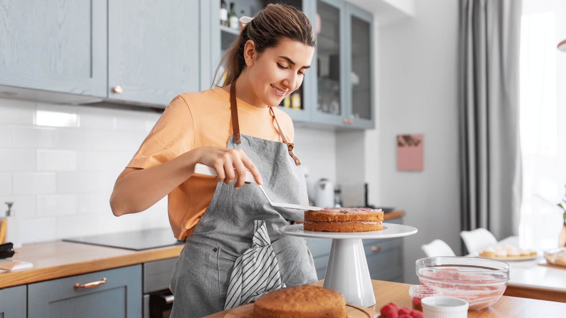 woman in gray apron baking cake and she frosts