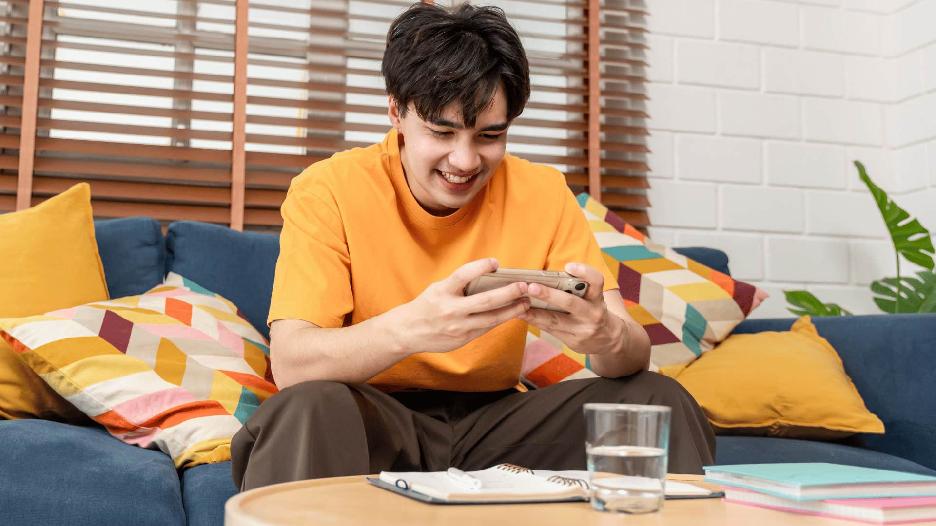man in orange shirt happy as he plays single player video game on couch