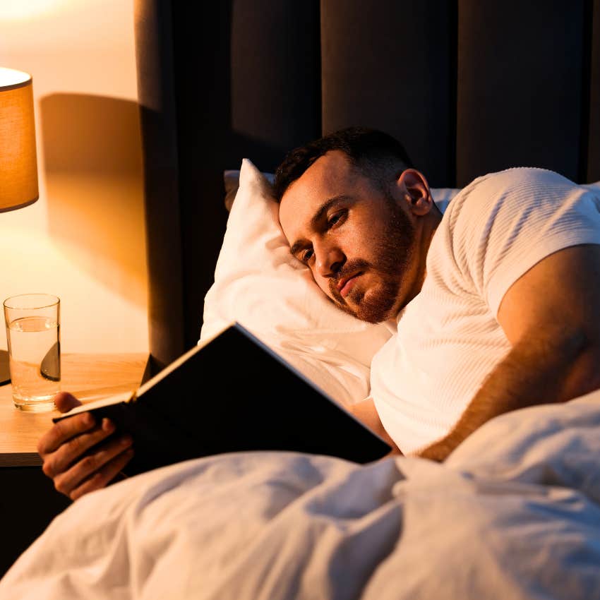 man reading a book in his comfortable bedroom at night