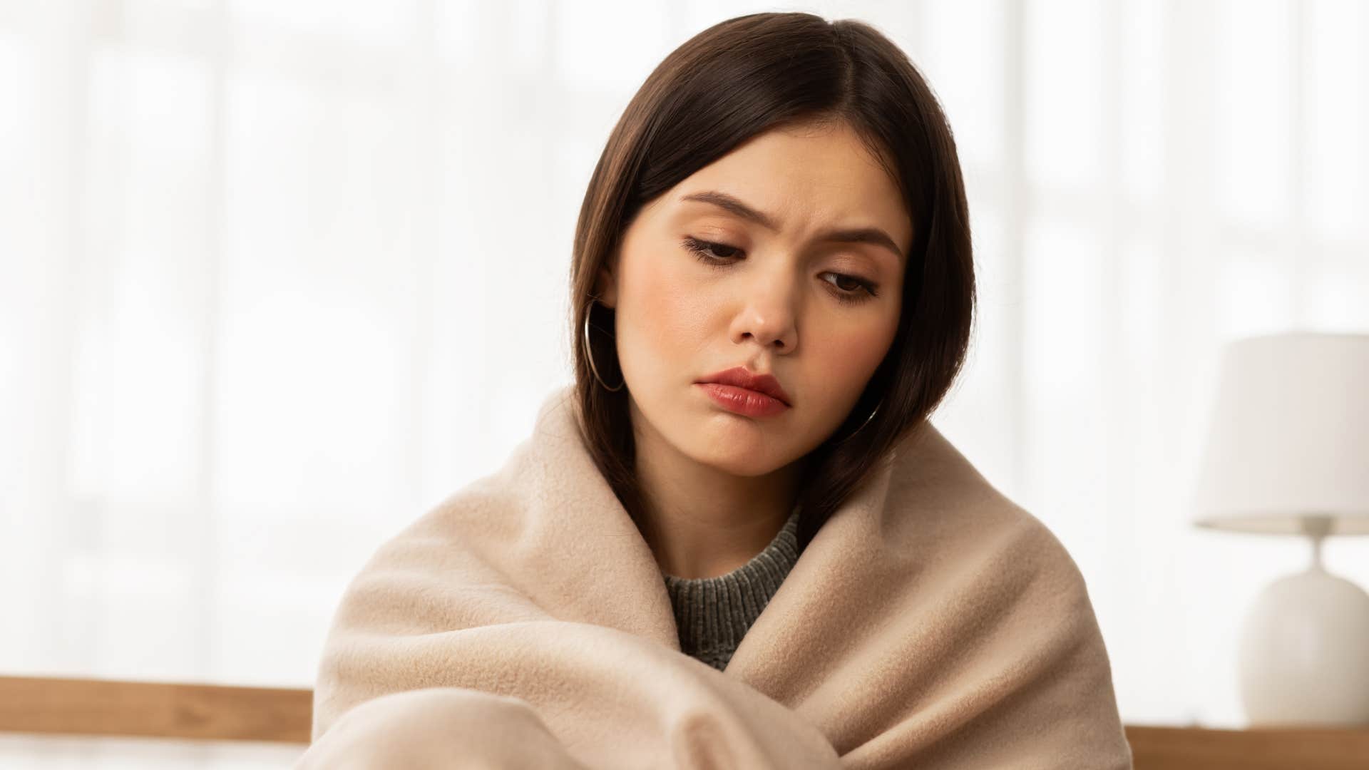 sad detached woman wrapped in a blanket saying i'm used to being alone