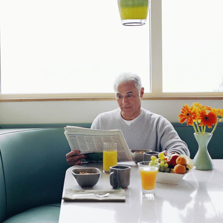retired man reading newspaper while eating breakfast