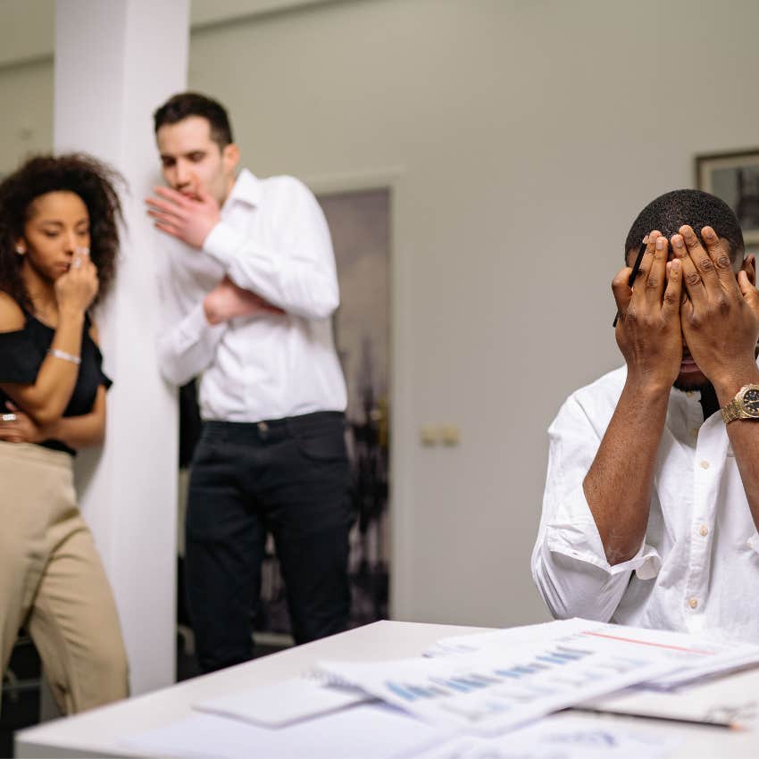 Professional employee standing apart from coworkers engaged in workplace gossip and office politics