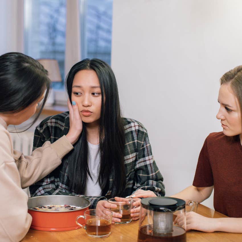 Woman seeming uncomfortable after talking to friends about relationship problems while her friends look concerned and disapproving