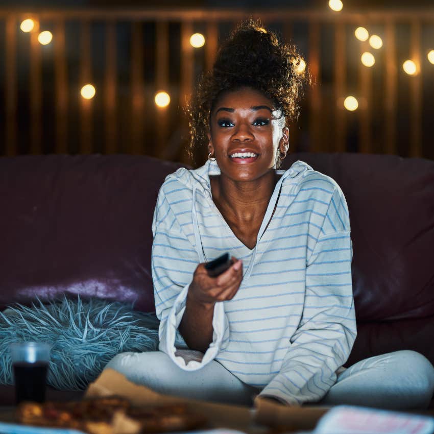happy introverted woman changing the channel on her television