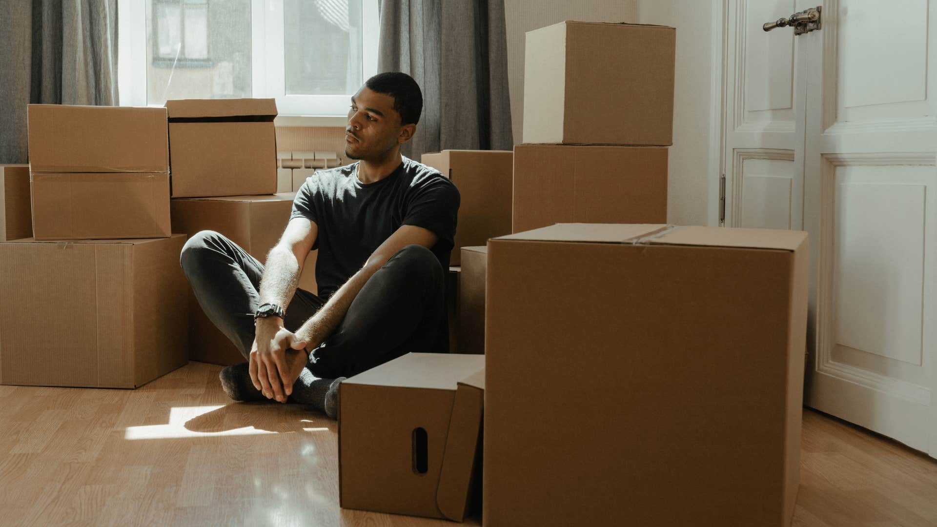 sad gen Z man sitting among moving boxes unable to afford a home
