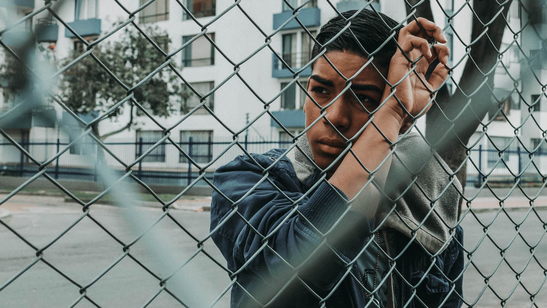 young Gen Z man feeling lonely standing by fence