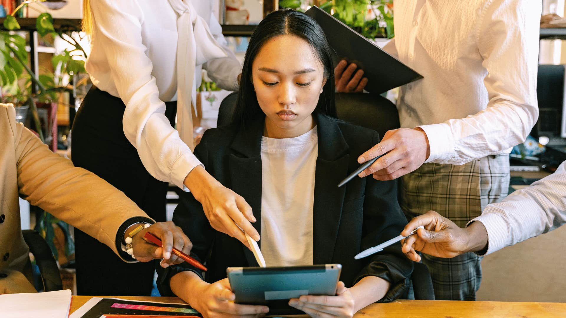 stressed gen Z woman at work surrounded by colleagues needing something