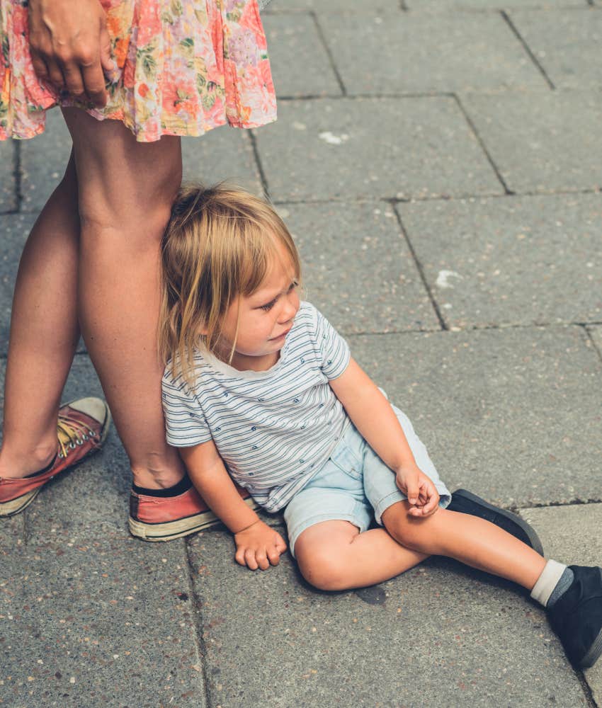 toddler having a meltdown leans against his millennial mom's leg