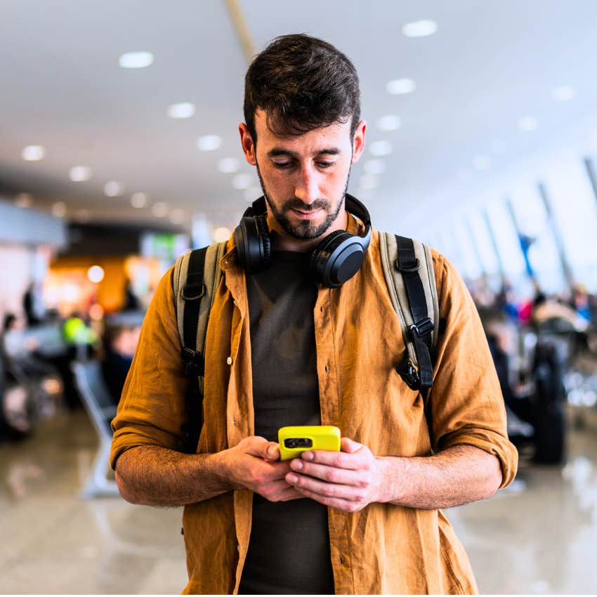 Gen Z man looking at his phone while he waits at the airport