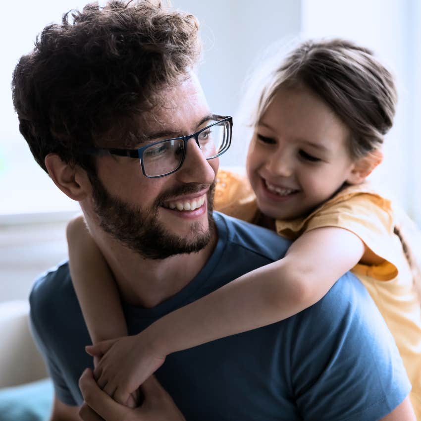 millennial dad giving his daughter a piggyback ride smiling