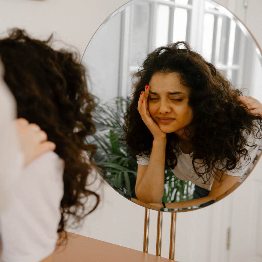 self-conscious woman looking unhappily at her reflection