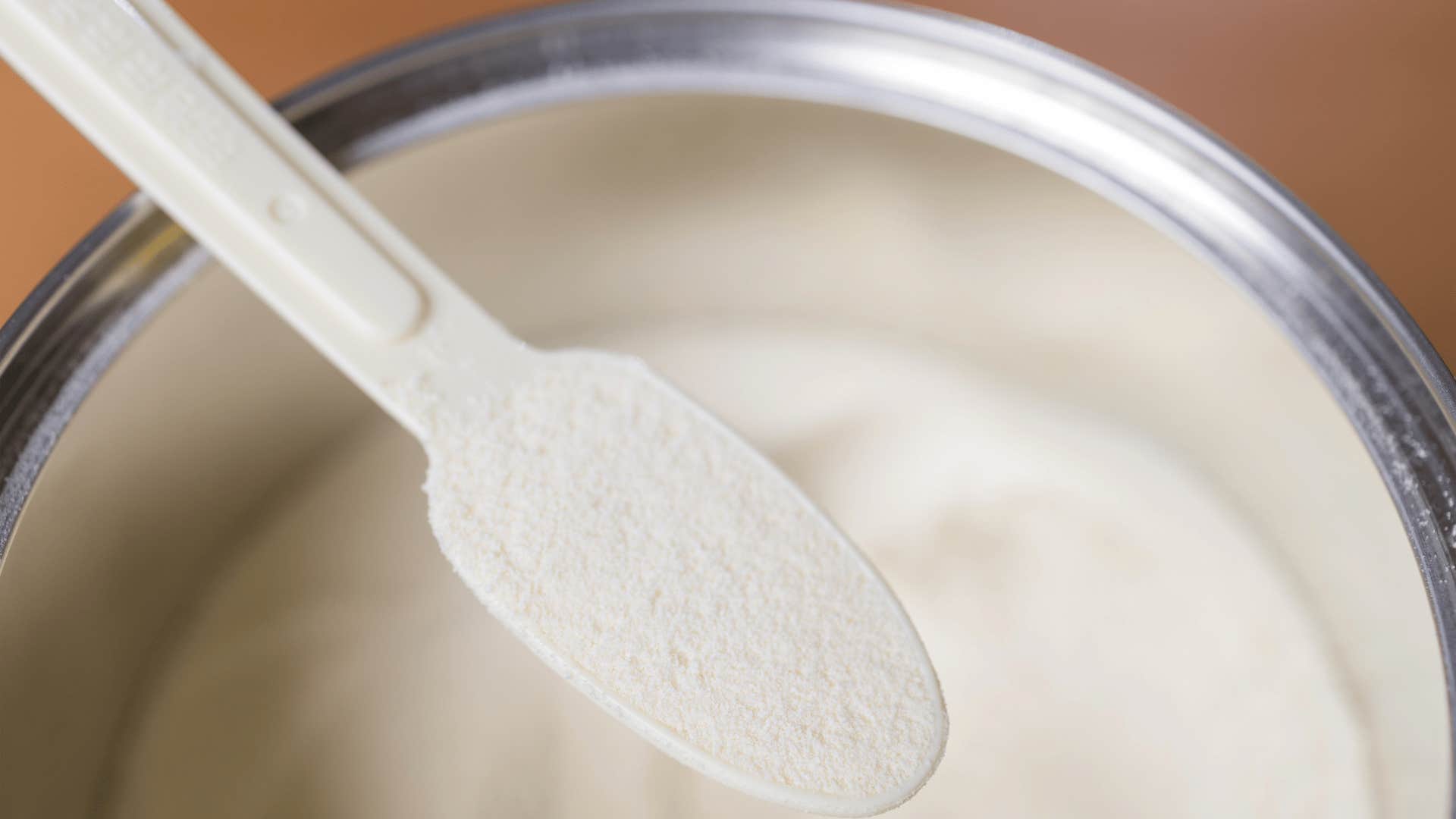 person scooping powdered milk with spoon from gray tin can