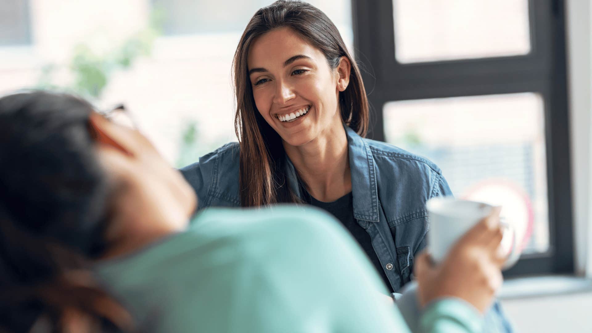 woman in jean jacket smiling as she sheepishly says sorry i'm talking too much