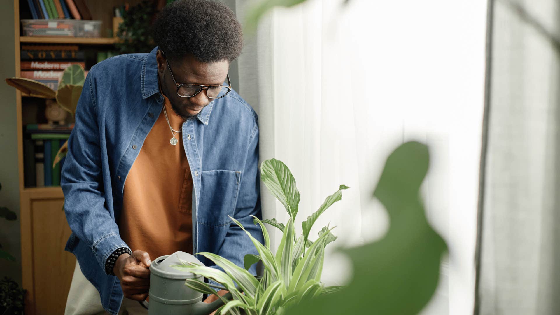 man in orange-brown shirt has houseplants he takes care of faithfully