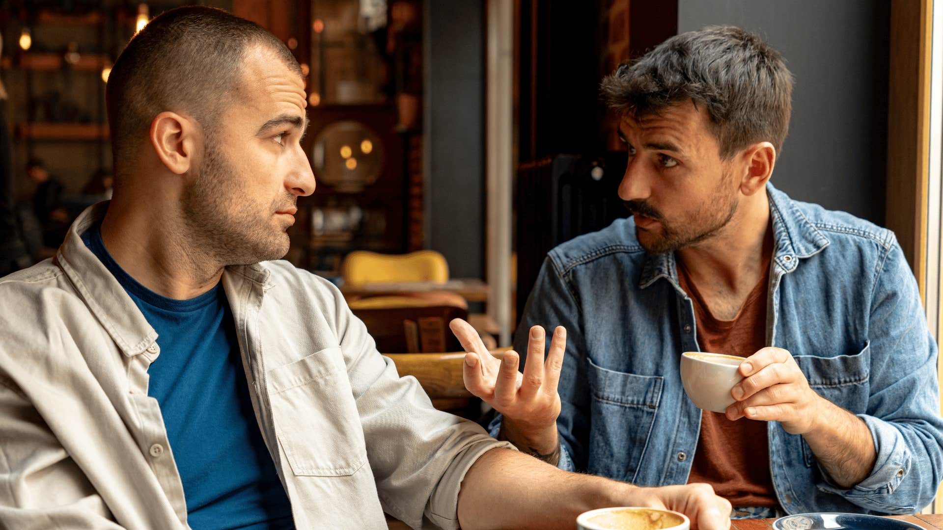 man in jean jacket at cafe pointing at friend as he tells him that's just the way people are
