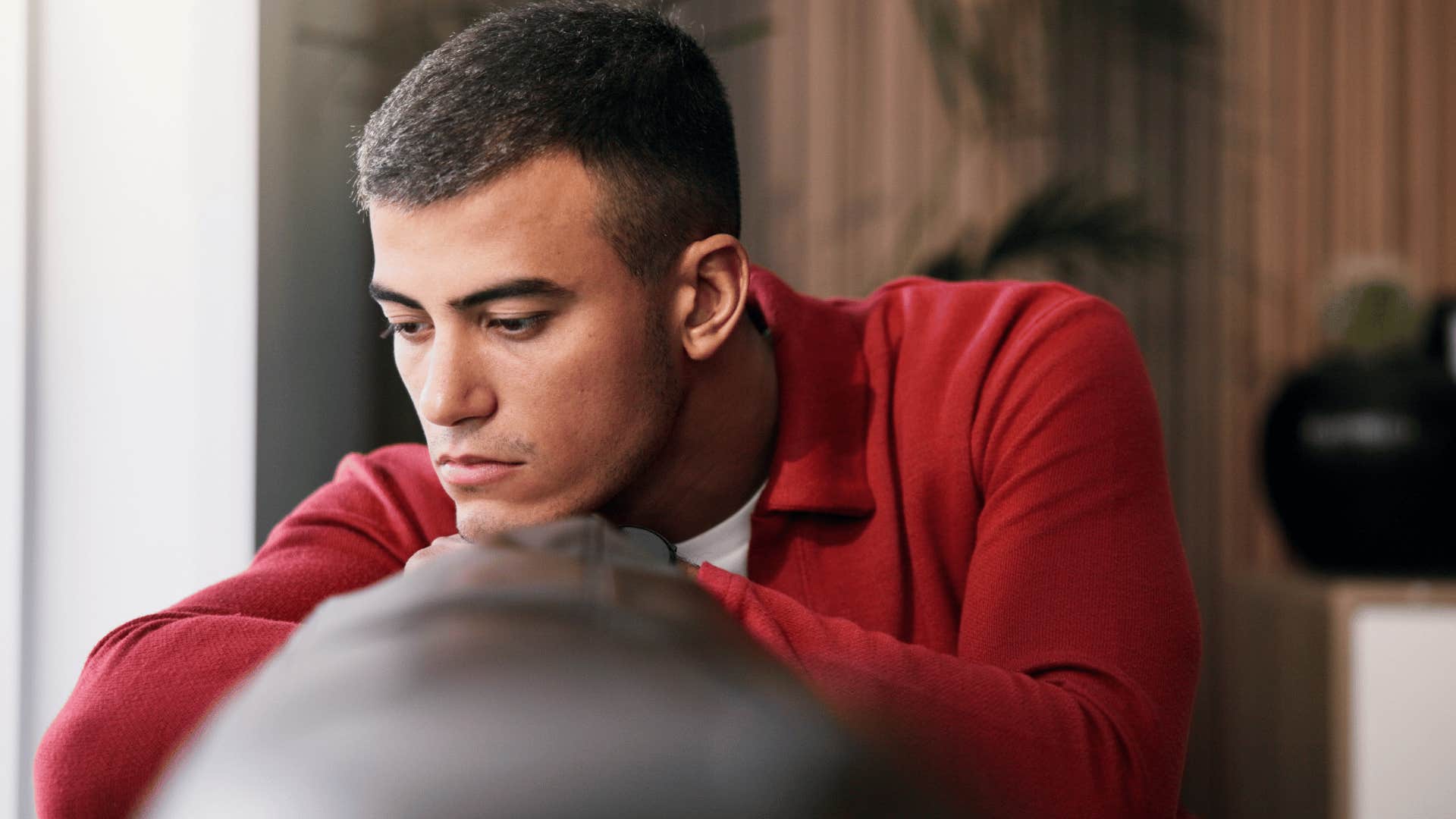 man in red shirt procrastinating on everything as he looks upset on couch
