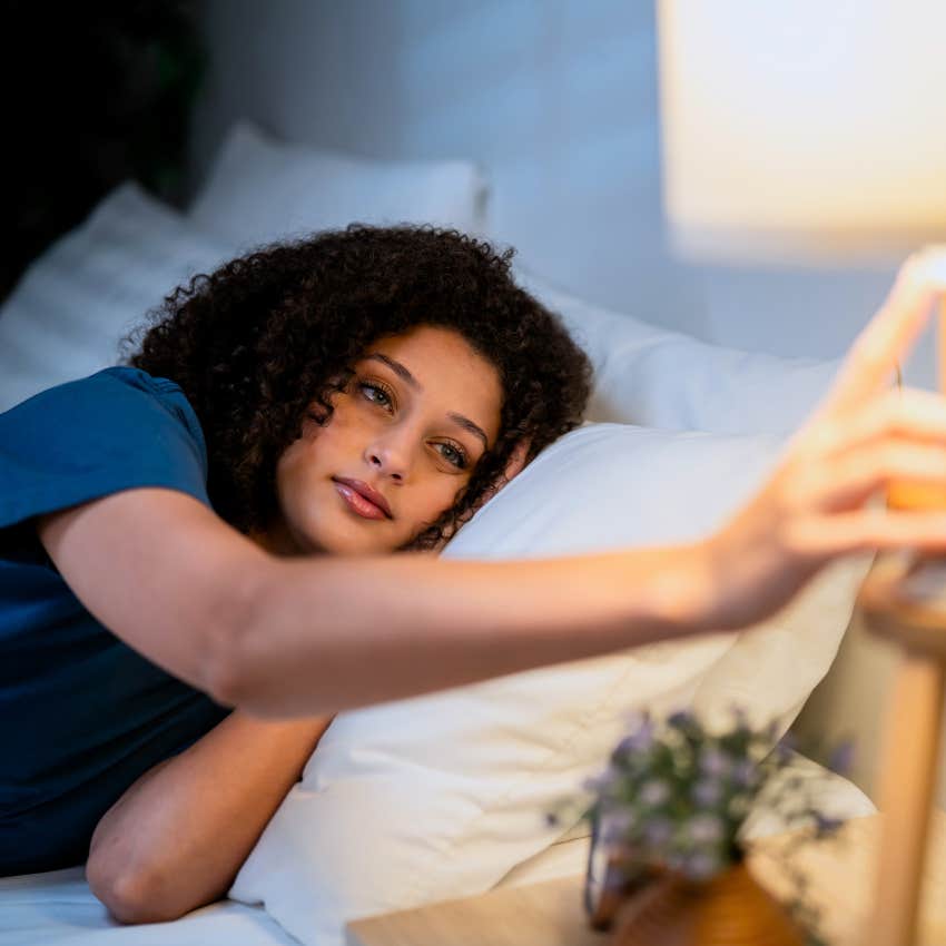 Woman who prefers being cozy in bed by 9 pm turning on ambient lighting