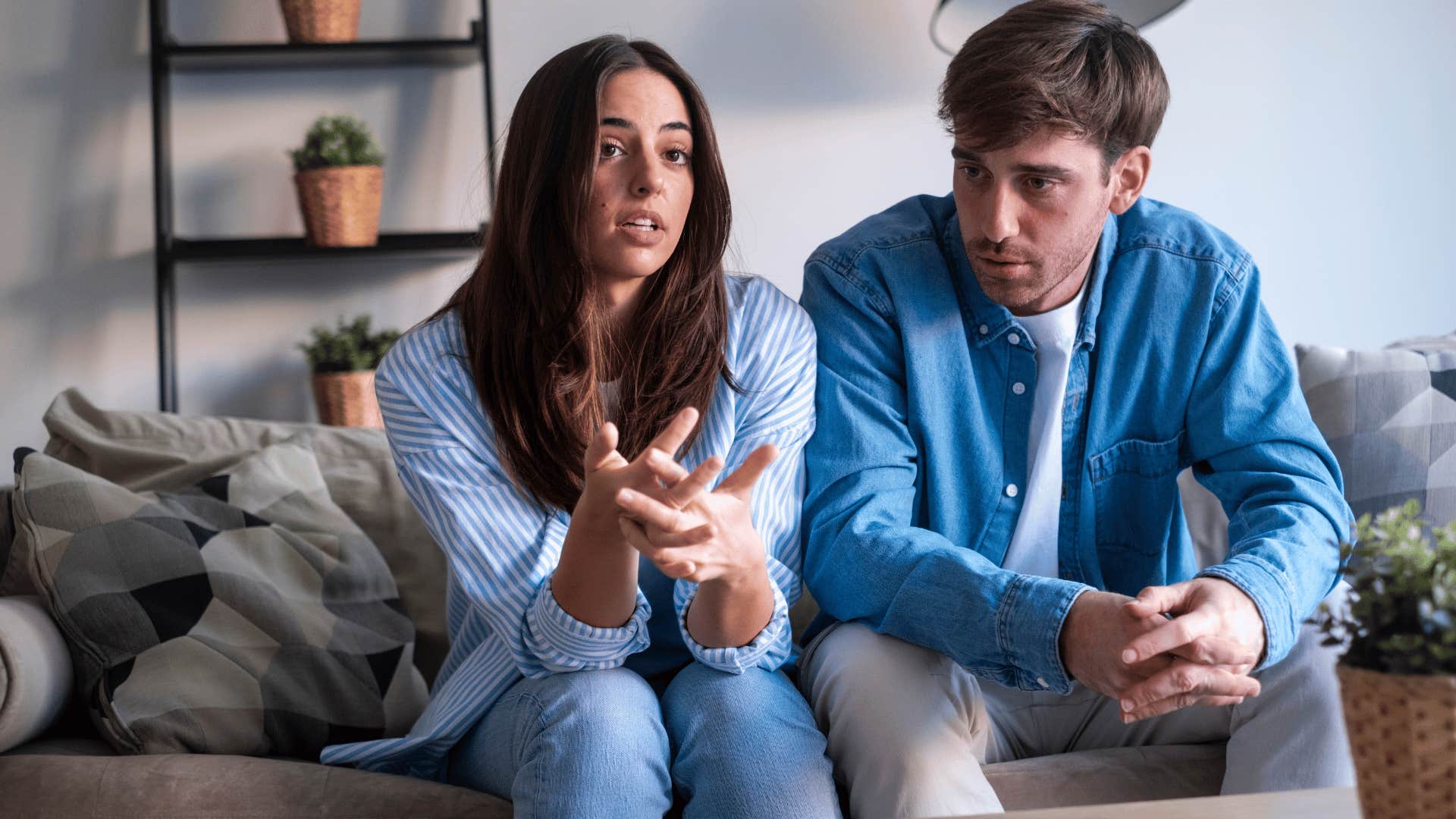 woman in blue shirt telling man it's probably my fault as they awkwardly sit on couch together