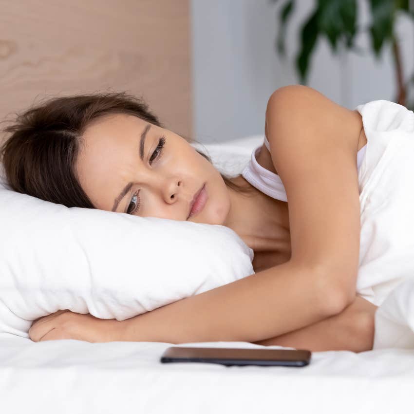 private woman lying in bed looking at text notification and annoyed