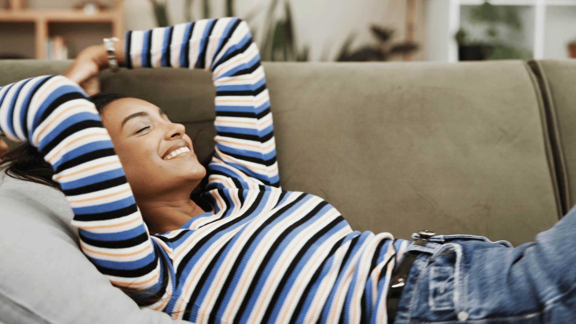 woman smiling brightly as she lays on the couch and thinks i'd rather stay home anyways