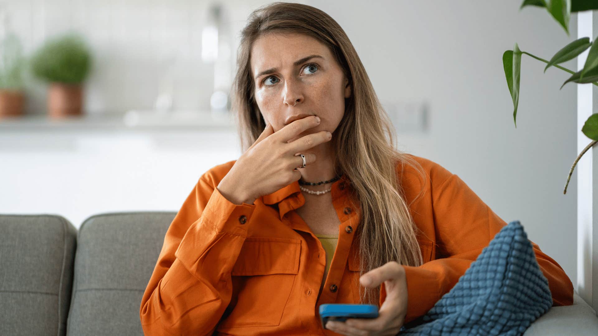 woman in orange shirt with phone in hand thinking i don't even know who i'd invite
