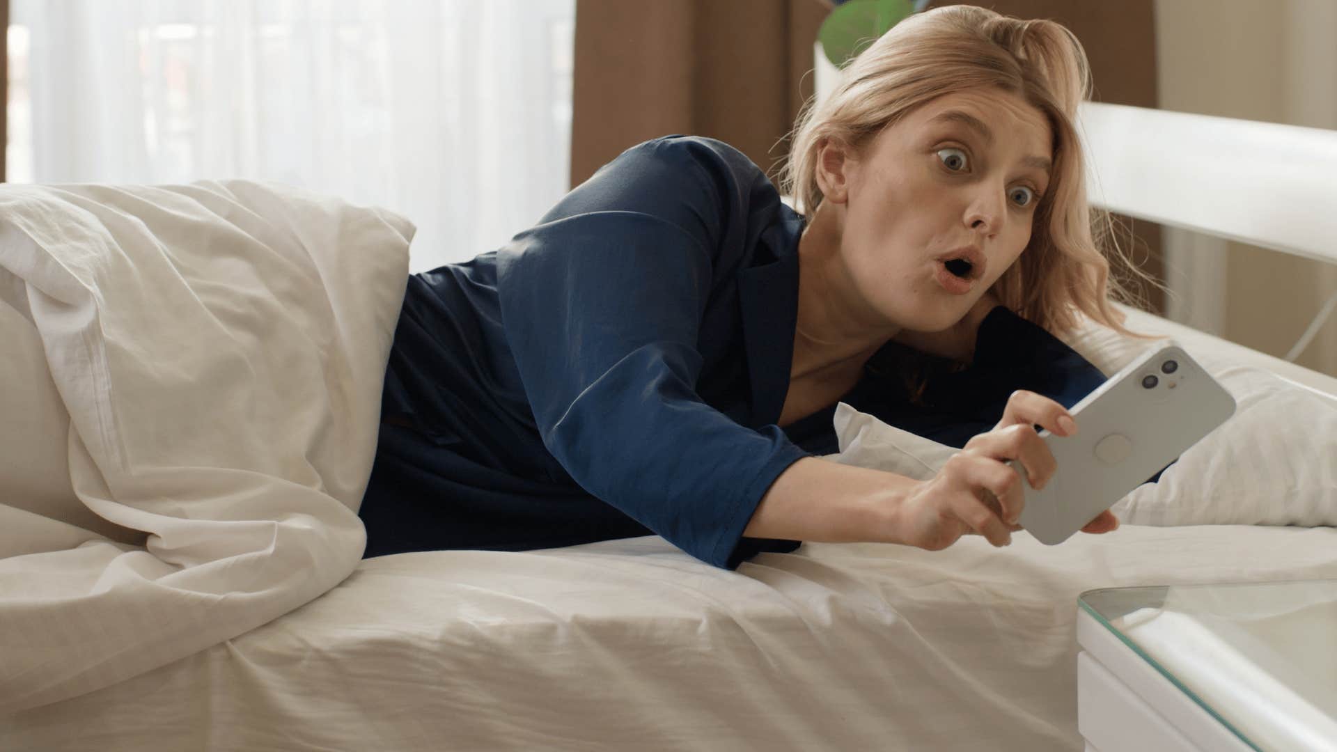 shocked woman looking at phone in bed